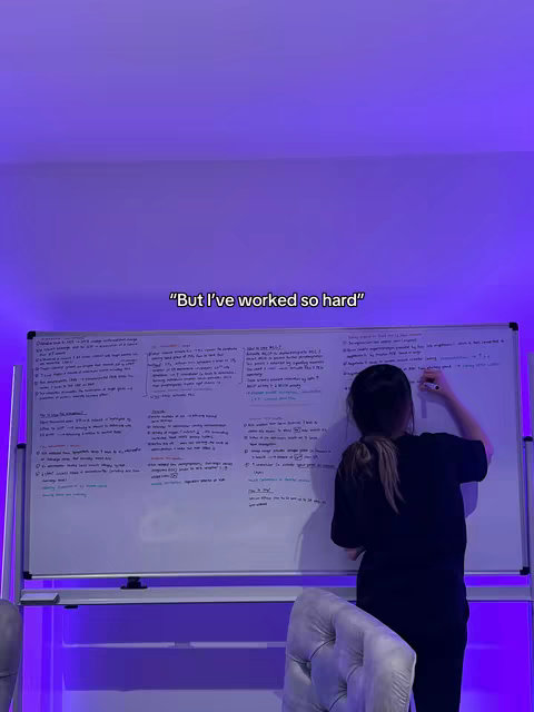 The cover image features a woman writing on a whiteboard, positioned in front of a wall lit with purple light. She is facing the whiteboard with her back towards the camera, dressed in a black t-shirt and with her hair tied back. Behind her is a light purple wall and what appears to be a velvet chair.