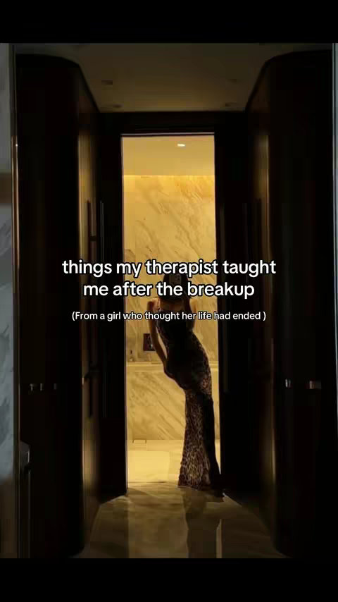The cover image features a woman standing in a doorway that leads to a bathroom. The woman is seen from the waist up, slightly angled towards the viewer, appearing in a long dress with a leopard print, and has long hair. The background subtly reveals a bathroom with marble finishes. The text overlayed at the top reads'things my therapist taught me after the breakup' and below that, the text reads '(From a girl who thought her life had ended)'.