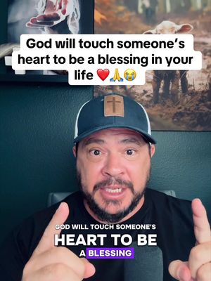 A selfie-style video featuring a man in a dark cap with a cross logo and a black shirt; overlaid text at the top reads a motivational message; in the background, a wall and two pictures are visible. The man gestures with both hands in the frame.