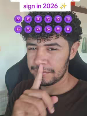 A man with an afro hairstyle wearing a brown shirt and holding a finger to his lips as a shushing gesture. Above his head, there are icons of zodiac signs.