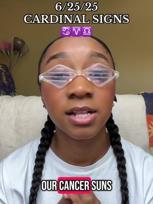 A young woman is centered in the frame, looking directly at the camera. She has her dark hair styled in two thick braids. She wears clear-framed, diamond-shaped glasses and a white t-shirt. Text overlays include the date '6/25/25' and 'CARDINAL SIGNS' above her and 'OUR CANCER SUNS' at the bottom, set against a pink backdrop. The background features a warm-toned wall, and decorative elements are visible on the left. The overall composition suggests a personal, informative video.