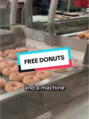 An industrial conveyor belt is filled with glazed donuts, with a text overlay that reads 'FREE DONUTS.' The image is taken at a slight angle, with the conveyor belt moving towards the viewer. The donuts are golden brown, with a shiny glaze. The text overlay is in a white font, with a rectangular background composed of cyan, black and red rectangles.