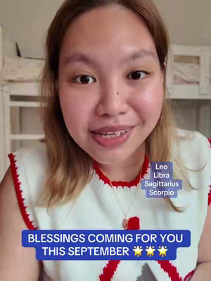 A young woman with light brown hair is centered in the frame, looking directly at the camera with a slight smile. She is wearing a white and red top and a necklace with a pendant. Overlaid on the image are text elements and boxes with astrological signs. The background is blurred, and appears to be a room setting.