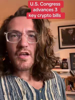 A man with glasses and wavy brown hair is centered. He is looking to the left of the camera with his mouth open. He is wearing a blue shirt. Text in a red rectangle at the top of the frame reads, 'U.S. Congress advances 3 key crypto bills'. A framed picture is visible on the wall behind him.