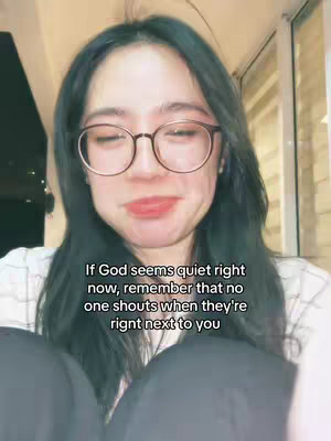 A woman wearing glasses is centered in the frame, looking slightly upwards with a soft expression. Text is overlaid, providing inspirational or religious content. The background is softly lit, suggesting an indoor setting.