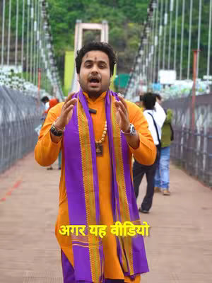 A man stands on a bridge, gesturing with his hands. He wears an orange shirt, a purple scarf, and a beaded necklace. Text overlays the image in yellow.