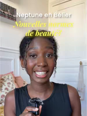 A woman with dark skin and curly black hair smiles at the camera, holding a microphone. Text overlays read, "Neptune en Bélier," and "Nouvelles normes de beauté?" The background is blurred, suggesting an indoor setting.