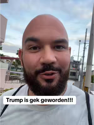 A close-up shot of a bald man with a trimmed beard looking directly at the camera. The man is outside, with a building and sky in the background. A text overlay at the bottom of the screen says 'Trump is gek geworden!!!'.