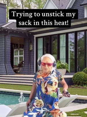 The image shows a person dressed as an elderly woman, wearing red sunglasses and headphones, sitting on a lounge chair by a pool. The woman looks directly at the camera. Behind her is a large modern house, adding to the setting. Text overlayed on the image says, 'Trying to unstick my sack in this heat!'.