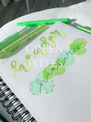 A flat lay image featuring a spiral-bound notebook open to a page with green lettering and watercolor accents. Several green highlighters are placed around the notebook on what appears to be a white surface. The text overlay reads 'GREEN TITLES'. The composition is clean and well-lit, with a focus on the stationery and the handwritten elements.