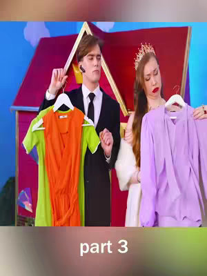 The image shows a scene from a video, likely a skit or a comedic scenario. A man in a black suit and a woman wearing a tiara and a white outfit frame a scene where they're each holding up clothing items, potentially outfits to choose from. The man holds out a lime green and orange dress, while the woman holding a light purple dress. They are standing in front of a cute decor of a miniature dollhouse.