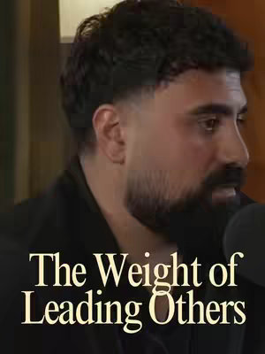 The cover image is a medium shot featuring a man in profile against a blurred background. The man has short, dark, curly hair with a neatly faded haircut on the sides. He has a beard and mustache, and is wearing a black jacket. Below him, text in a cream-colored font reads "The Weight of Leading Others". The background is blurred, with indistinct objects and colors.