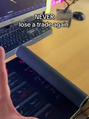The cover image shows a setup of a professional workspace for trading. It features a desk with a keyboard, computer monitor displaying trading graphs, and a mouse. A rolled-up black mousepad sits near the foreground with a computer screen in the background. Above, the text overlay reads 'NEVER lose a trade again'. The lighting suggests a well-lit indoor setting.