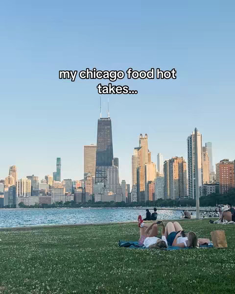 The image shows a scenic view of a Chicago skyline with Lake Michigan in the foreground. The skyline is a mix of various skyscrapers, featuring the iconic Willis Tower. In the foreground, there are people lying on the grass, and a clear blue sky forms the backdrop.