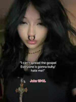 A young woman with long, dark hair and facial piercings is centered in the frame, looking directly at the camera. Text overlays are visible, stating a quote and a Bible verse reference. The background is slightly blurred, suggesting an indoor setting. The overall composition is close-up and centered, with the subject as the primary focus.