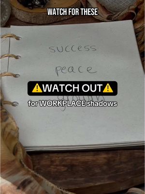 An open notebook is shown, with the words 'success' and 'peace' handwritten on one of the pages. A black rectangular banner with yellow exclamation point symbols and the words "WATCH OUT for WORKPLACE shadows" in white is overlayed over the bottom of the image.