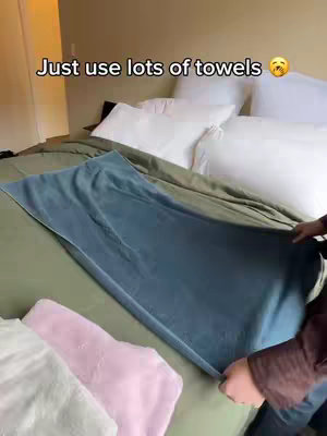 A bed with white pillows, green sheets, and a blue towel is seen. A person is holding the towel. Text overlay is also present.