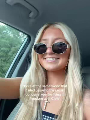 A woman with long blonde hair and sunglasses smiles at the camera, sitting in the driver's seat of a car. The background includes the car's interior and a glimpse of greenery through the window, and text overlay on the image.