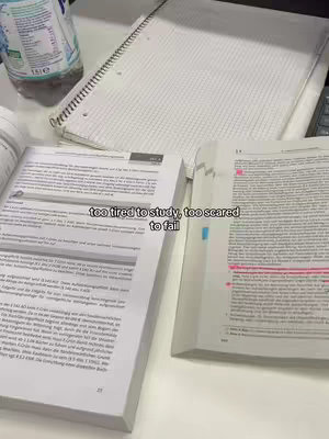 A top-down shot of a desk covered in study materials. Open books and a spiral notebook dominate the scene, suggesting an environment for focused study. A bottle of water adds a touch of realism to the setting.