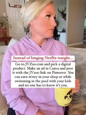 A medium shot features a blonde woman sitting on a beige couch, with a light pink hooded sweatshirt and silver earrings. She appears to be mid-sentence, looking to her left with a slight frown. In the background, a glimpse of a decorated room is visible, which includes a dark-colored deer head wall mount and a white door. An overlaid text is present on the bottom of the image with a call to action: "Instead of binging Netflix tonight... Go to JVZoo.com and pick a digital product. Make an ad in Canva and post it with the JVzoo link on Pinterest. You can earn m'ney in your sleep or while swimming in the pool with your kids and no one has to know it's you."