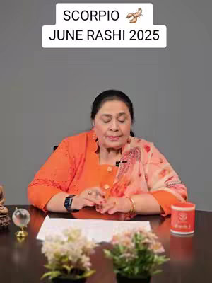 A woman in an orange jacket and patterned shawl sits at a table. She looks down, hands clasped. A white rectangle with text floats above her, and flowers and a small globe decorate the table.