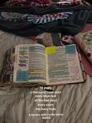 An open bible is lying on a bed, with text written on the right page and sticky notes. Above the bible are patterned blankets.