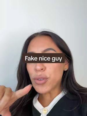 A woman with long dark hair, wearing a white top under a black jacket, points her finger towards the viewer. A dark brown rectangle obscures the center of her face, displaying the text, "Fake nice guy".