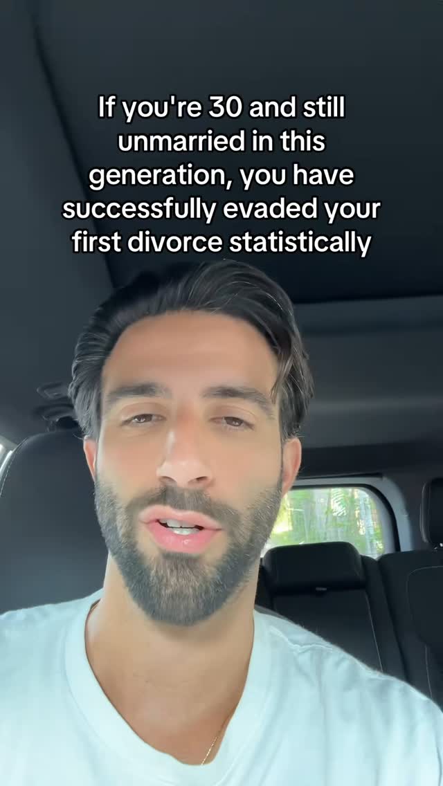 A man with dark hair and a beard is filming from inside a car. Text overlayed on the car window states 'If you're 30 and still unmarried in this generation, you have successfully evaded your first divorce statistically'.