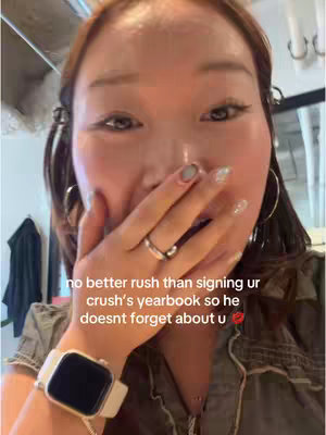 A close-up selfie shows a young woman covering her mouth with her hand, appearing surprised or shy. The woman is fair-skinned, with long black hair, and is wearing ear rings, a white watch, and a shirt. Text overlays the image in a casual, handwritten-style font.