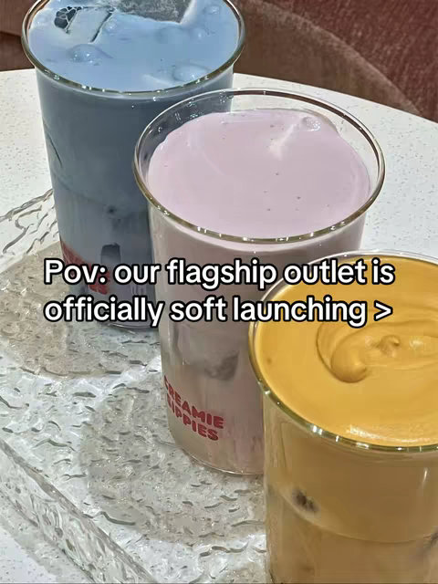 The image shows three glasses of colorful drinks against a blurred background. The drink on the left is light blue, the middle drink is pink, and the right one is yellow. The glasses sit on a surface with a textured design, and the text overlay is white, centered at the bottom.