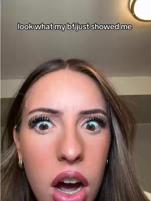 Close-up shot of a woman with wide eyes and an open mouth, conveying surprise or shock, with a text overlay stating 'look what my bf just showed me.' The lighting appears to be soft, possibly from indoor lighting.