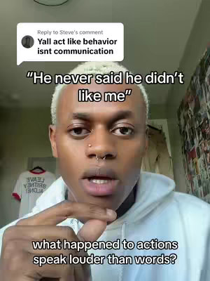 A selfie-style video cover image featuring a Black man with blonde highlights, wearing a white hoodie. He's looking towards the camera with a subtle expression and a nose piercing. Text overlays include a comment bubble with a response and a quote below. The background is blurred but appears to be indoors. The overall composition is focused on the man's face with simple background.
