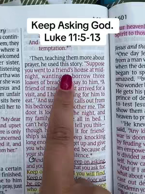 The image shows an open Bible on a wooden surface. A hand with a red nail is pointing to a section of the text. Text overlay at the top says: Keep Asking God. Luke 11:5-13.