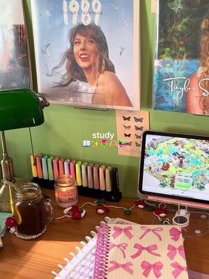 A desk setup with study supplies. There are posters of Taylor Swift, colorful highlighters, a lit candle, a jar of tea, and an iPad.