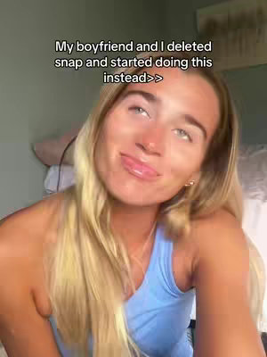 A young woman with long blonde hair looking up and to the side, with a slight smile and a playful expression. She is wearing a blue tank top. The background is a soft, neutral tone, possibly a wall.
