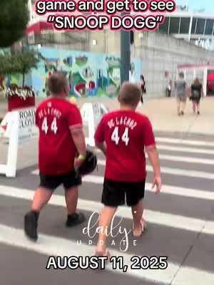 Two boys, viewed from the back, are walking along a crosswalk. They are wearing red shirts with the number "44" on the back. Text overlays at the top say "game and get to see 'Snoop Dogg'". The bottom features additional text with a  "daily update" title and the date "AUGUST 11, 2025".