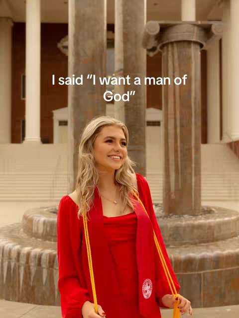 A young woman in a red dress and graduation stole smiles in front of a fountain and classical architecture. Text is layered at the top.