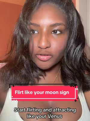 A selfie-style shot features a Black woman with long, wavy dark hair, looking towards the left. She is wearing a white tank top and a delicate necklace. The image has two overlaid text boxes: one red rectangle across the center that reads "Flirt like your moon sign", and one below it the text "Start flirting and attracting like your Venus".