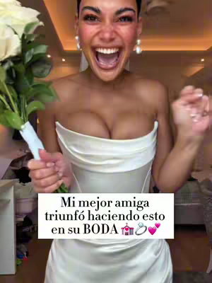 A woman, with dark hair pulled back, wearing a white strapless dress and holding a bouquet of white roses. She is enthusiastically smiling and has her mouth wide open. A text overlay in white reads, "Mi mejor amiga triunfó haciendo esto en su BODA" with a wedding cake, ring, and heart emojis.