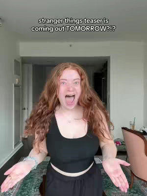 A woman with long, wavy red hair is centered in the frame, her mouth wide open in an expression of excitement. The background shows a living space with doors and a chair, indicating an indoor setting. Text overlays at the top communicate a message.