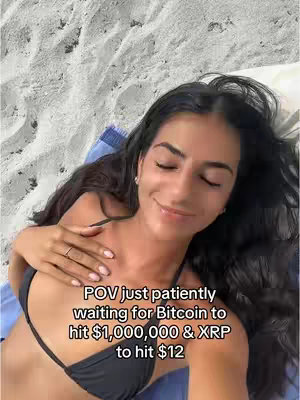 A woman with long dark hair lies on her side on a sandy beach, resting her head on a blue towel. She's wearing a black bikini top and has her eyes closed, hand resting on her chest. The background is blurred, showing the sand texture and reflecting sunlight, creating a serene and relaxed atmosphere with warm tones