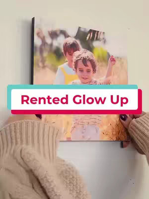 A woman's hands are holding up a photo print with two children in it against a plain white wall. A teal and white banner with the text "Rented Glow Up" is overlayed near the bottom.