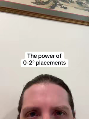 A selfie-style shot taken from approximately the midpoint of a person's face, captured from the mid-forehead down. The person's expression is neutral. Positioned above the person is a white text overlay that reads, "The power of 0-2° placements".

In the background, there is a structured decorative element or painting. The overall composition includes the person's features in the foreground, the text in the middle ground, and a background design.