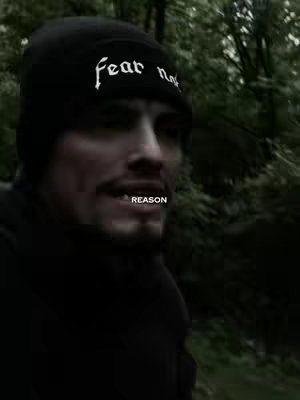 A man wearing a black beanie with the words "fear not" in white on it, standing in a forest setting with blurred background, and the word "REASON" in white at the bottom.