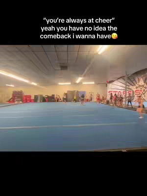 The cover image is a wide shot of a cheerleading gym, focused on the blue mat on the floor. In the background, some people are standing, but the video is mainly focused on tumbling. The text overlay starts close to the top left of the frame.