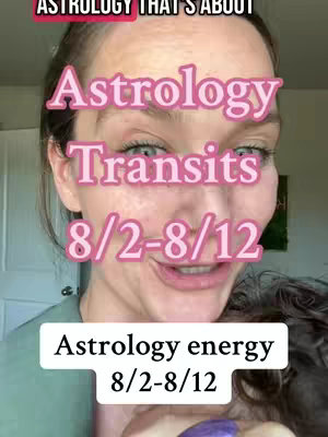 A close-up shot of a woman with a light background. Overlaid on her face are large pink text overlays spelling out "Astrology Transits 8/2-8/12" in a bold font. Below, another white text box says "Astrology energy 8/2-8/12". The woman is smiling with makeup and has her hair back in a messy style and is holding a purple object in front of her face.