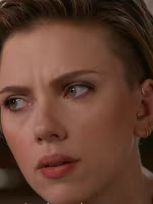 Close-up shot of actress Scarlett Johansson's face, looking contemplative or emotional. She is turned slightly to the side, with her gaze directed off-screen. Her expression is serious, with a subtle furrow in her brow. She has fair skin, with what appears to be small gold hoop earrings. The background is out of focus, suggesting a shallow depth of field. The composition is tightly framed, highlighting her facial features and expression.