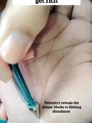 A close-up shot of a hand, presumably holding a pen, with palm lines visible. A pen is held over the palm, seemingly pointing towards a particular line.