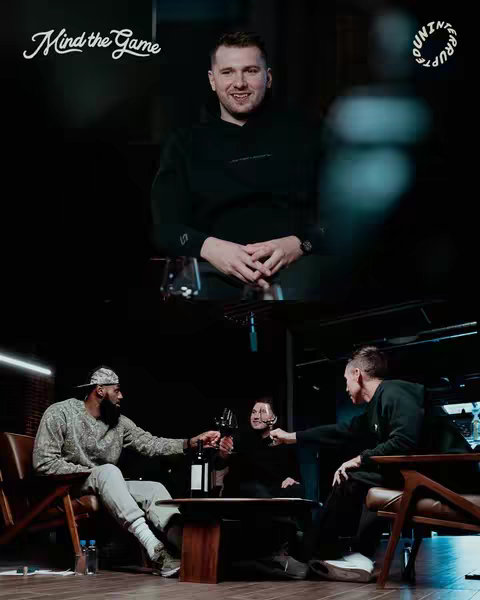 The cover image displays a split-screen arrangement. The top portion of the image captures a well-lit interior with a man, presumably Luka Dončić, positioned in front of a textured black background. Below, three men, including LeBron James and possibly Steven Nash, are seated together in a well-lit setting, engaged in a toast with glasses of wine, set against a dark backdrop.