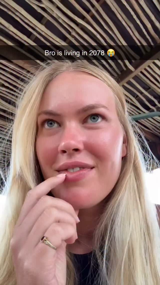 The cover image features a close-up shot of a woman with long blonde hair and blue eyes, looking upwards with a thoughtful expression. Her finger is near her lips. The background shows a thatched roof structure with a pattern of light and dark brown lines. The overall composition is a casual, selfie-style shot.
